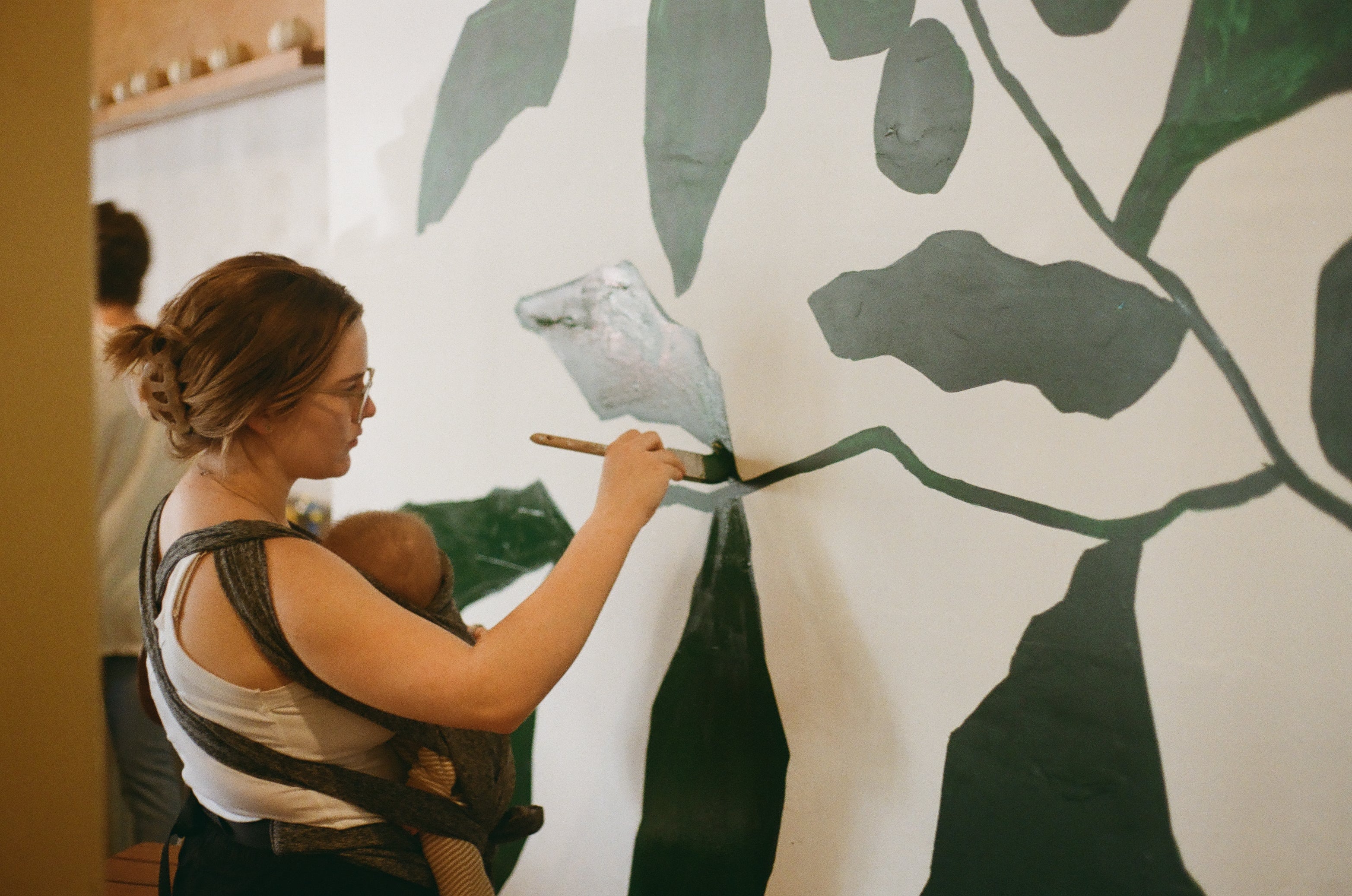 Woman painting a large abstract design on a wall with green and black colors.