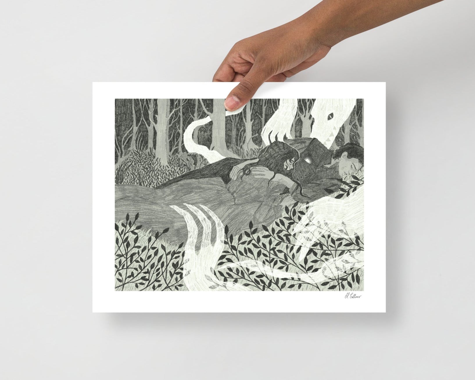 Hand holding a framed artwork of a forest scene with a path and animals.